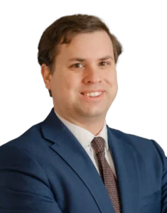 A man in a blue suit and patterned tie poses for a professional portrait, smiling with arms crossed against a neutral background, representing Fairfax family law lawyer services.